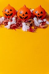 Halloween orange pumpkins on a background of yellow, decorated with red autumn leaves and little ghosts, copy and paste space