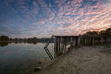 Autumn landscape on the river at dawn, where the sun is rising on the horizon and the sky is pink...