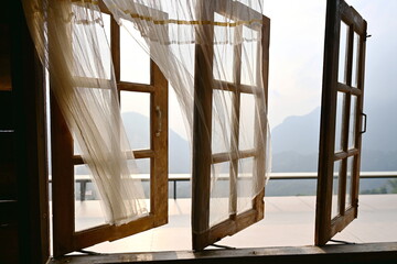 The glass windows are draped with airy or thin white cotton curtains that are blown away by the...