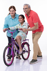 Obraz premium Indian grandparents assisting cheerful granddaughter in riding bicycles on white background.