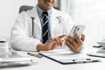 Fototapeta premium Male doctor working on desk with smarrtphone and laptop computer and paperwork in the office. Medical and doctor concept.