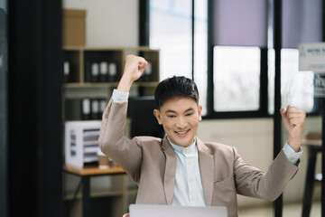 Successful business man, excited young man Keeping up arms and showing positive emotions, happy working in modern office on computer.
