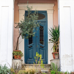 A classic design house entrance with a blue painted door and potted plants. Travel to Athens, Greece.