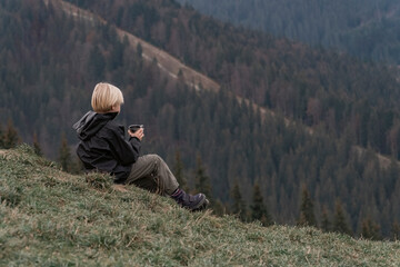 Naklejka na ściany i meble Blond boy in mountains resting on hillside with cup of tea. Hiking with child. Active recreation or vacation