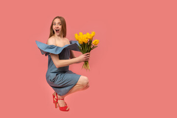 Surprised Caucasian young woman in sundress in sandals with heels holding bouquet of yellow flowers...