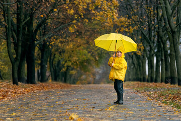 Boy smiling with large yellow umbrella in hands in the autumn park. Rainy fall day