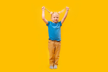 Cheerful preschooler wears blue T-shirt on yellow background. Full-length portrait of little girl with two ponytails