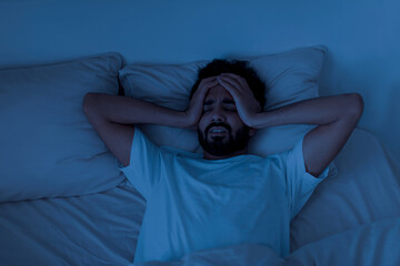 Sleeping Problem. Stressed young indian man lying in bed and touching head