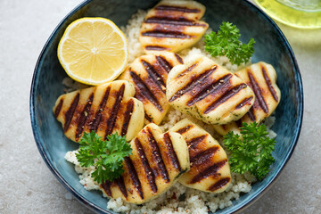 Slices of grilled haloumi cheese served with couscous in a blue bowl, horizontal shot, middle closeup