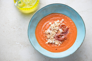 Turquoise bowl with salmorejo or chilled spanish tomato and bread soup, elevated view on a light-beige stone background, horizontal shot