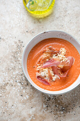 Bowl of spanish salmorejo cordobes on a beige stone background, vertical shot with space, high angle view