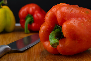 Three peppers with a knife on a wooden chopping board. Bell peppers of various colors on a wooden cutting board on a black background.