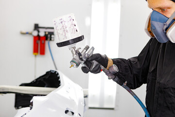 Close-up of spray gun with red paint painting a car in special booth

