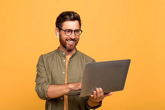 Professional IT specialist. Middle aged businessman holding laptop typing and working online, standing on yellow background