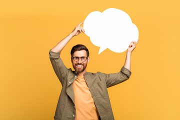 Happy european middle aged man in casual outfit holding blank conversation bubble over his head on yellow background