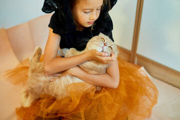 Little girl in Halloween costume with cat at home.
