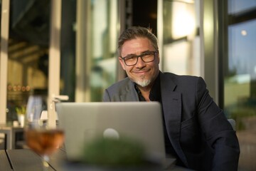 Happy businessman with laptop computer in restaurant. Middle aged man sitting at table in hotel lobby or business lounge in office, working, smiling. - 639835432