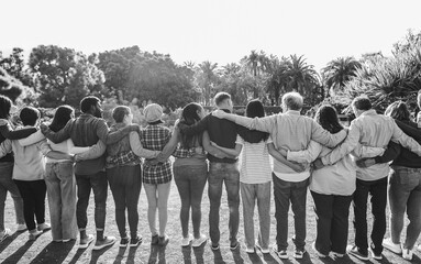 Group of multigenerational people hugging each others - Support, multiracial, inclusion and diversity concept - Main focus on center people - Black and white editing