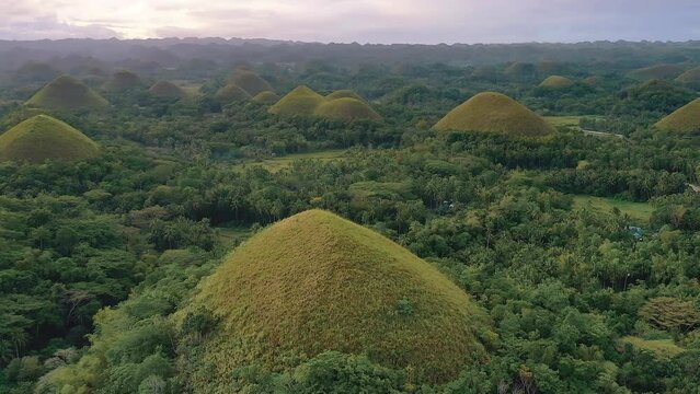 Chocolate Hills at sunset in Bohol Island, Philippines. Aerial drone cinematic shot. Slow upwards revealing view. Famous tourist landmark. Vibrant dusk colors and dramatic cloudy sunset.