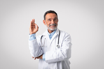 Glad caucasian senior doctor therapist in white coat show ok hand gesture, approving health care