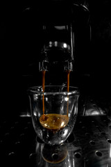 Coffee falling through the double spout filling into a glass cup with foam and bubbles from an automatic espresso machine with the background in black and white