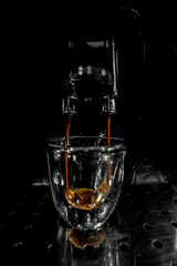 Coffee falling in motion frozen by the double spout filling into a glass cup with foam and bubbles from an automatic espresso machine with the background in black and white