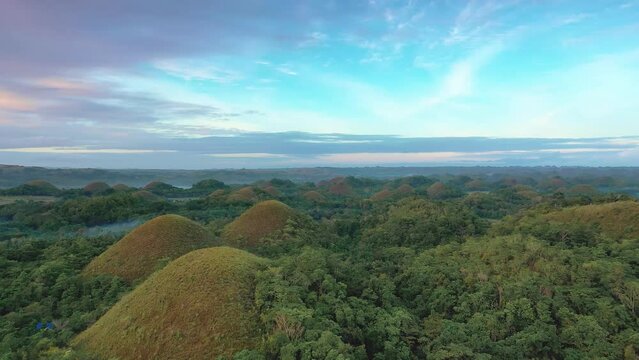 Chocolate Hills at sunset in Bohol Island, Philippines. Aerial drone cinematic shot. Slow travelling above famous landmark. Vibrant colors and cloudy sunset.
