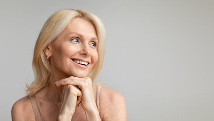 Attractive middle aged woman with hydrating glowing skin looking aside at free space and smiling,...