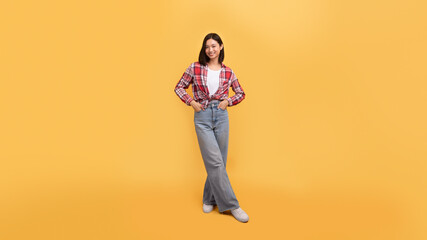 Full length shot of happy lady in casual outfit posing holding hands in pockets and smiling at camera, yellow background © Prostock-studio