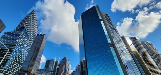 Naklejka premium Downtown, skyscrapers in Sydney, below view. Huge buildings, highrise towers, blue cloudy sky.