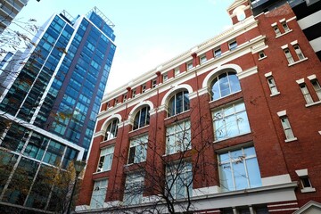 Obraz premium A reddish building with arched windows trimmed in white, a dry tree in front of the building, and a bright blue sky, Melbourne, Australia