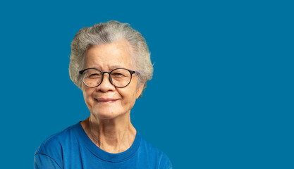 Beautiful senior woman with short white hair and glasses smiles at the camera while standing against a blue background.