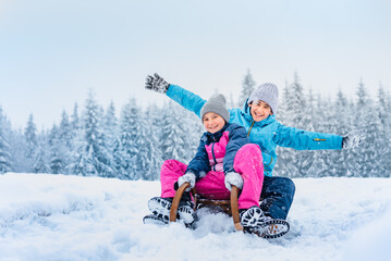 Family are sledding. Happy children run on wooden sleds down the slope. Winter sports entertainment for children. Wonderful snowy landscape background.