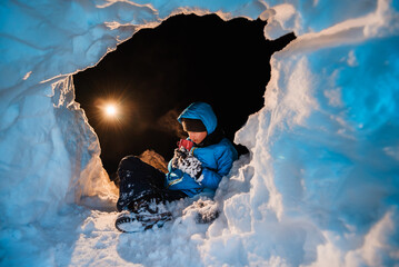 Survivor warms himself with mug of hot drink in snow shelter at night. Child was lost in mountains....