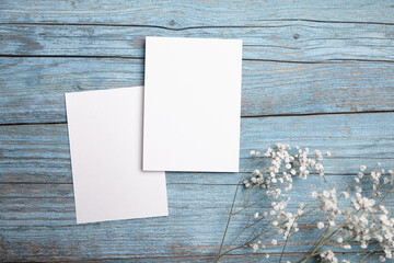 Blank invitation card mockup, two white greeting cards with dried flowers on blue wooden...