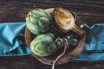 Artichoke close up. Fresh raw organic green Artichokes in a wood plate, closeup. Over wooden table,...