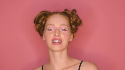 Close-up portrait of a smiling woman with braces on her teeth on pink background.