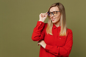 Young smiling minded fun woman she wearing red shirt casual clothes touch glasses looking aside on workspace area mock up isolated on plain pastel green background studio portrait. Lifestyle concept.