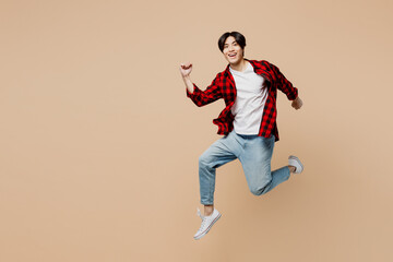 Fototapeta na wymiar Full body side view young excited cheerful happy man of Asian ethnicity wear red shirt casual clothes jump high run fast look camera isolated on plain pastel light beige background. Lifestyle concept.