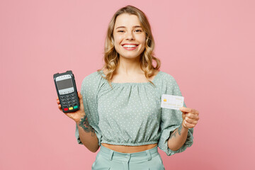 Young smiling happy woman in casual clothes hold wireless modern bank payment terminal to process acquire credit card isolated on plain pastel light pink background studio portrait Lifestyle concept