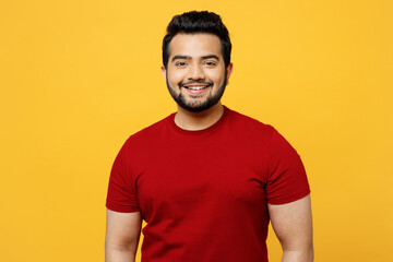 Young smiling satisfied positive cheerful optimist happy Indian man he wearing red t-shirt casual clothes looking camera isolated on plain yellow orange background studio portrait. Lifestyle concept. - obrazy, fototapety, plakaty