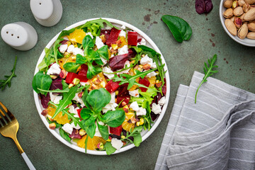 Beet and feta cheese salad with arugula, lettuce, orange and pistachios on green table. Fresh useful dish for healthy eating