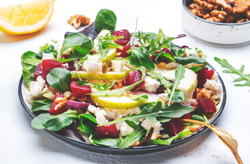 Beetroot, feta cheese and pear salad with arugula, lettuce, red onion, swiss chard and walnut, white kitchen table. Fresh delicious dish for healthy eating