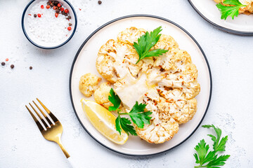 Vegan steak from baked cauliflower with garlic butter, parley and spice on plate, white table background, top view