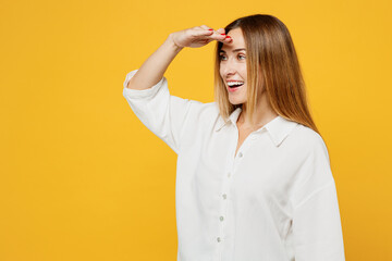 Young smiling fun cool caucasian happy woman she wears white shirt casual clothes hold hand at forehead look far away distance isolated on plain yellow background studio portrait. Lifestyle concept.