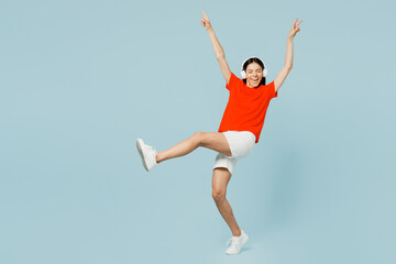 Fototapeta premium Full body side view young latin woman wear orange red t-shirt casual clothes listen to music in headphones raise up hands dance isolated on plain pastel light blue cyan background. Lifestyle concept.