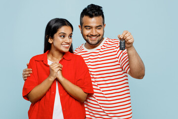 Full body smiling happy young couple two friend family Indian man woman wear red casual clothes t-shirt together hold in hand car keys fob keyless system isolated on plain blue cyan color background.