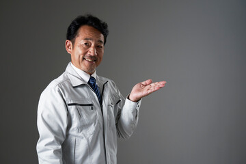 右側を手のひらで指すミドルエイジの作業員　黒背景