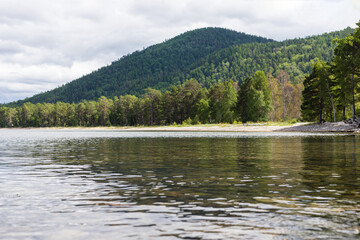 A picturesque summer landscape with a reflection of mountains and forests in the calm blue water. Chivyrkuisky Bay of Lake Baikal.Zabaikalsky National Park, Buryatia,Russia.Summer natural landscape.