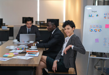 Attractive young confident businesswoman sitting at the office table with a group of ethnic colleagues in the background,